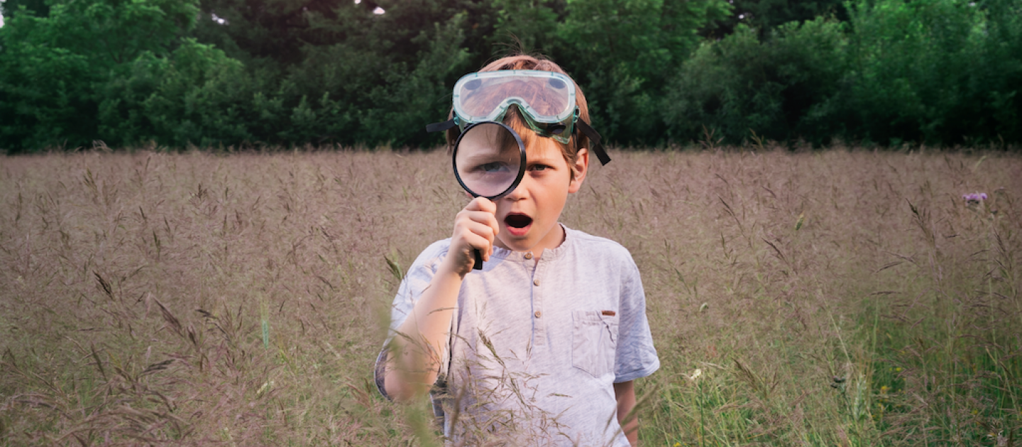 Een jongen met een vergrootglas in een veld met hoog gras